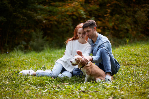 Щаслива любляча пара розслабляється на траві погладжуючи собаку
 - Фото, зображення