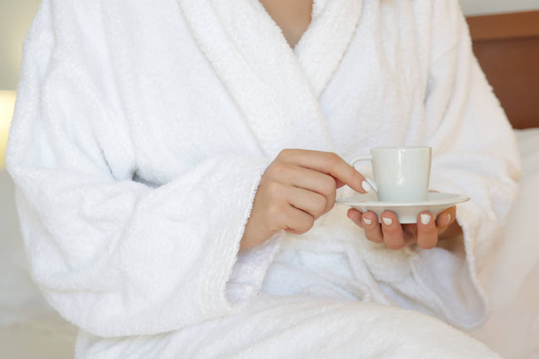 Frau im weißen Bademantel bei einer Tasse Kaffee im Schlafzimmer - Foto, Bild