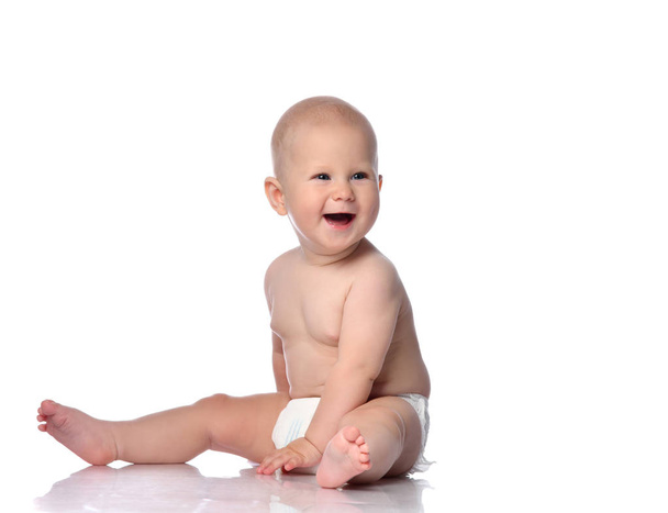 Laughing infant child baby boy toddler in diaper is sitting  looking aside at free copy space on white  - Photo, Image