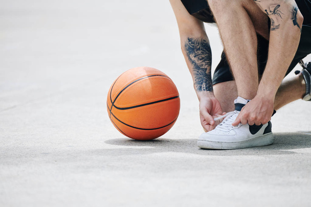 Κοντινή εικόνα μπασκετμπολίστα που δένει αθλητικά παπούτσια σε υπαίθριο γήπεδο - Φωτογραφία, εικόνα