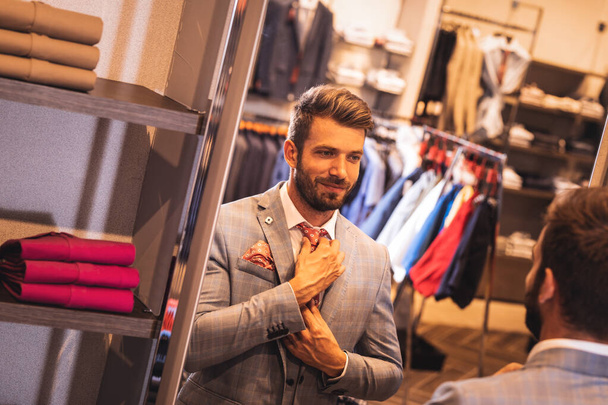 Elegant look. Handsome man in suit adjusting his tie while stand - Foto, imagen