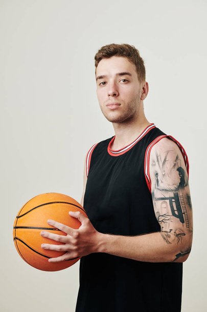Portrét seriózního profesionálního basketbalisty s míčem v ruce při pohledu do kamery  - Fotografie, Obrázek