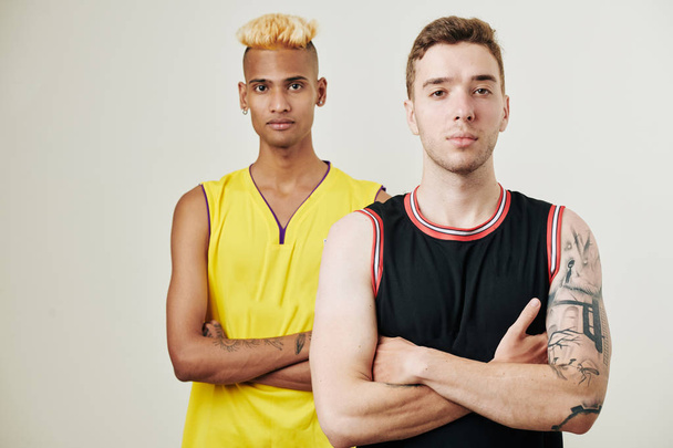 Retrato de estudio de jugadores de baloncesto multiétnicos confiados parados uno detrás del otro y mirando a la cámara
 - Foto, imagen