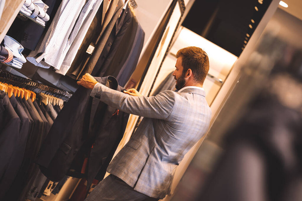 Young man choosing suit in clothes store. - Photo, Image