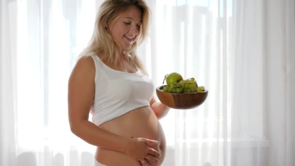 Ernährung während der Schwangerschaft: Weibchen mit dickem Bauch isst Trauben von einem Holzteller - Filmmaterial, Video