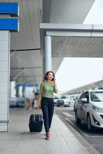 Smiling pretty girl using mobile phone and looking into distance. Lady with suitcase concept - 写真・画像
