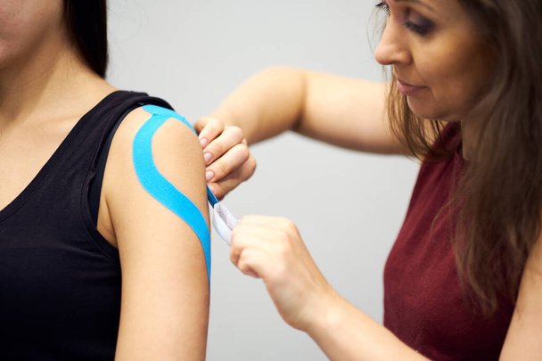 tratamiento con cinta adhesiva cinesiológica con cinta azul en el brazo lesionado de la paciente. Lesiones deportivas tratamiento kinesio
 - Foto, Imagen