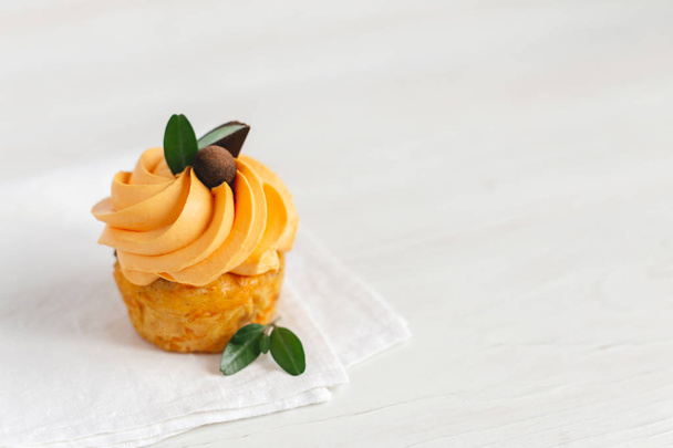 Tasty pumpkin cupcake with orange cream and decoration on white wooden table. - Photo, Image