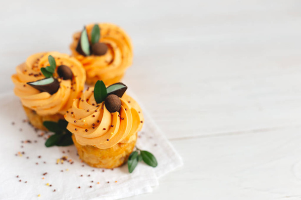 Finom sütőtök muffinok narancssárga krémmel és dekoráció fehér fa asztalon.  - Fotó, kép
