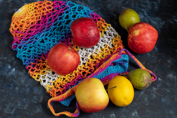 Ecological cotton mesh for carrying and storing products. Durable, bright. Fruits lie in and near her. Apples, pears, lemon. View from above. On a bright background.  - Foto, Imagem
