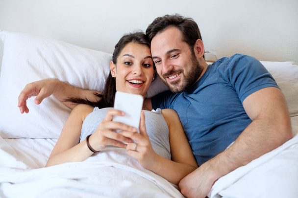Coppia innamorata nel letto tenendo smartphone
 - Foto, immagini