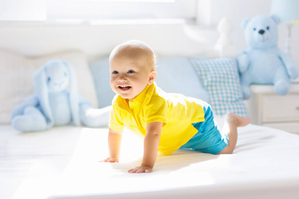 Baby boy playing on bed in sunny nursery - Fotó, kép