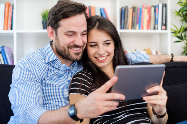 Cheerful couple using a tablet on line sitting in the living roo - Foto, Imagem