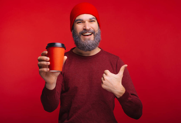 Photo of happy man holding cup of coffee to go and showing thumbs up - Photo, Image