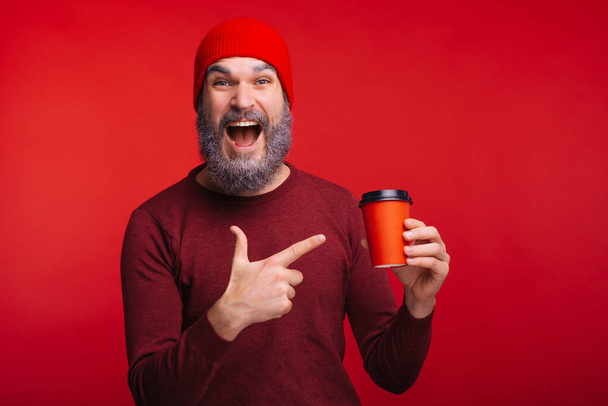 Csodálkozó férfi fehér szakállal, piros csésze kávéra mutatva. - Fotó, kép