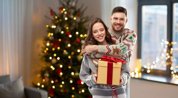 happy couple in christmas sweaters with gift box - Valokuva, kuva