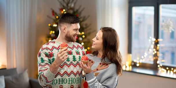 couple with cupcakes in ugly christmas sweaters - Fotó, kép