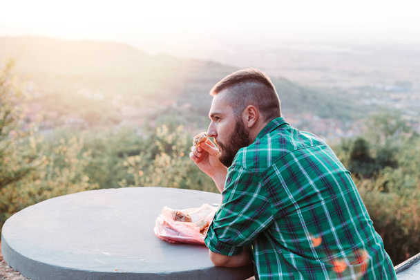 Cute, bearded guy eating some pie, resting on the bench - Photo, Image