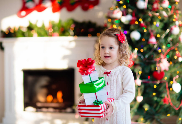 Pikkutyttö avaa joululahjoja takassa
 - Valokuva, kuva