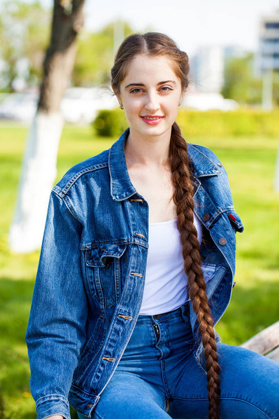 Beautiful girl in a denim jacket sits on a bench in a summer par - Fotografie, Obrázek