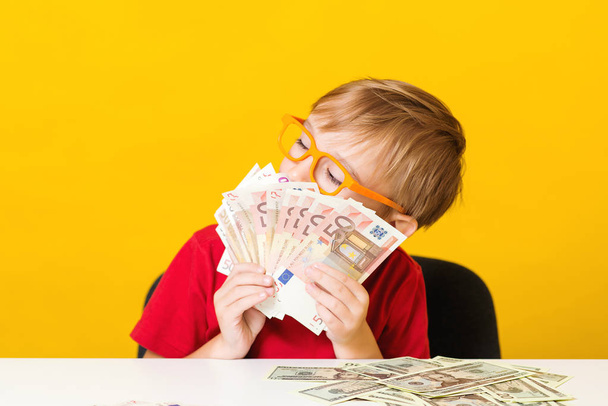 Cute little boy holds a lot of money. Kid save money for future education. Money, finances, insurance and people concept - Photo, Image