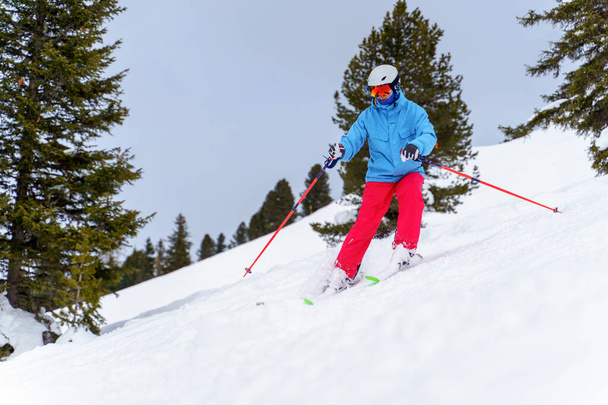 Foto van sportman in helm skiën in wintersportplaats vanaf besneeuwde piste - Foto, afbeelding