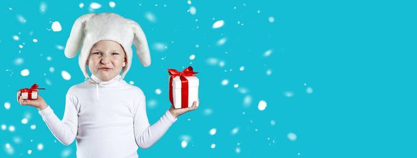 a boy dressed as a white hare tries to choose a gift on blue background - Fotoğraf, Görsel