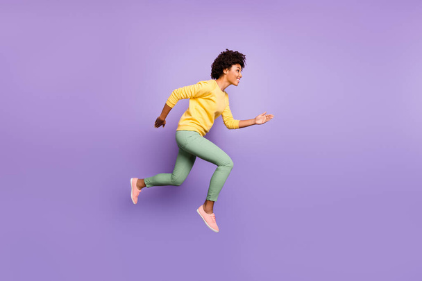 Full body profile side photo of positive brunette curly hair dark skin girl hear news fall spring discounts jump run wear yellow pullover green pants trousers isolated violet purple color background - Fotoğraf, Görsel
