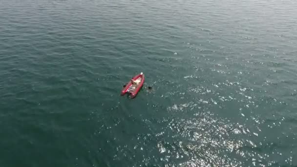 Vista aérea. Barco vermelho puxa dois mergulhadores para fora da água, longe em mar aberto
 - Filmagem, Vídeo