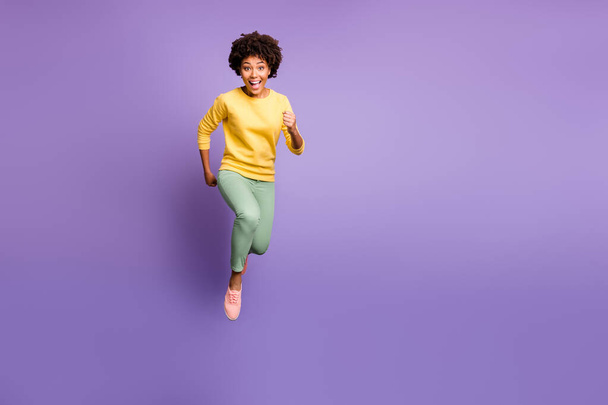 Discounts i come. Portrait of funky crazy afro american girl jump run hurry get autumn black friday bargain wear yellow sweater green pants trousers sneaker isolated violet purple color background - Фото, зображення