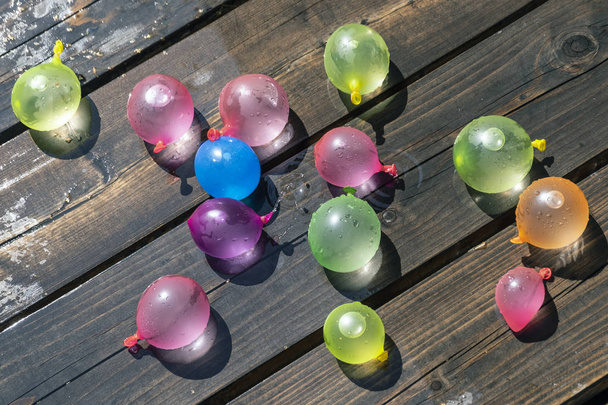 Bunte aufblasbare Gummibälle zum gegenseitigen Werfen, als Kinderspaß. mit Wasser gefüllt und auf einem hölzernen Hintergrund liegend. - Foto, Bild