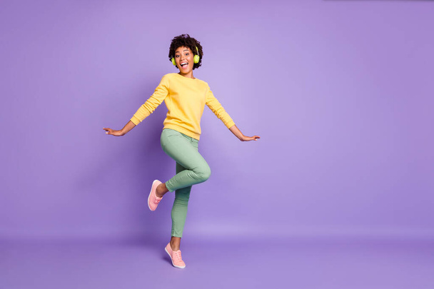 Full length body size turned photo of cheerful positive cute nice charming girlfriend dancing in headphones wearing yellow sweater green pants trousers isolated over violet pastel color background - Φωτογραφία, εικόνα