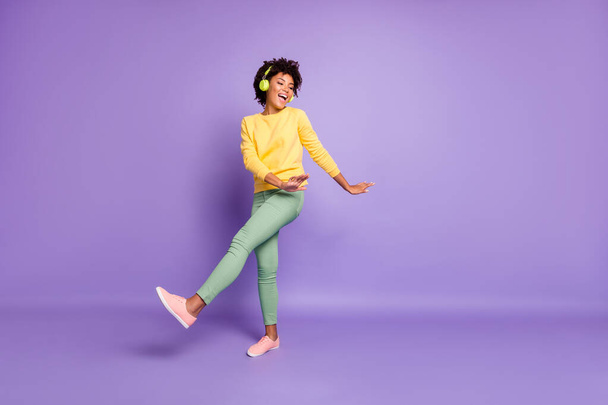 Full length body size photo of cheerful wavy curly haired sweet pretty girl of freedom wearing green pants trousers dancing listening to her music out of headphones isolated over violet color pastel - Foto, Imagen
