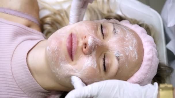 Kosmetyk kładzie krem na twarz kobiety w salonie piękności. - Materiał filmowy, wideo