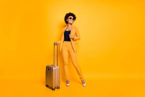 Full size photo of positive cheerful girl hold trolley package ready to enjoy free time on vacation wear stylish fashionable outfit pants footwear isolated over yellow color background - Foto, immagini