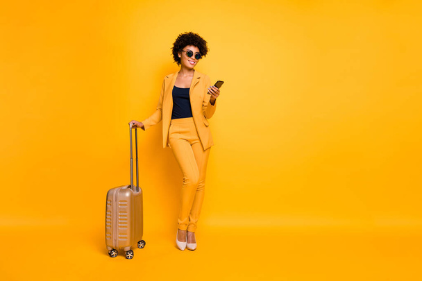 Full size photo of focused brown wavy hair tourist girl use smartphone hold bag try book taxi reach destination on autumn weekends wear jacket pants high-heels isolated yellow color background - Fotoğraf, Görsel