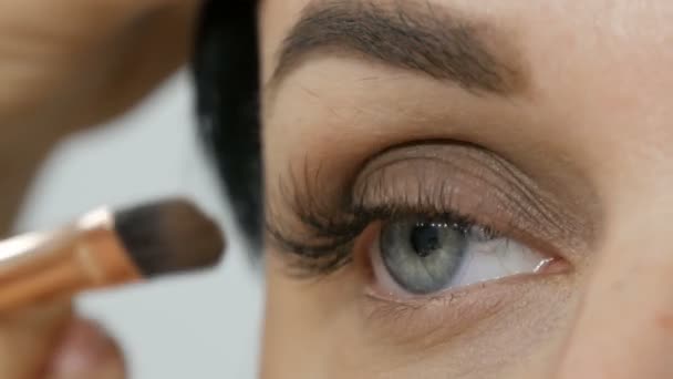 Detailní pohled na krásné ženské modré oko s prodlouženými řasami. Make-up malíř aplikuje make-up pomocí speciálního obočí a štětcem oční stíny na krásný model. Profesionální high fashion. - Záběry, video