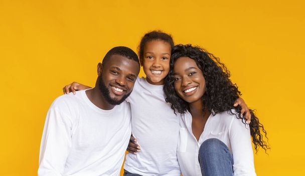 Glimlachende Afro-Amerikaanse vader, moeder en dochter over gele achtergrond - Foto, afbeelding