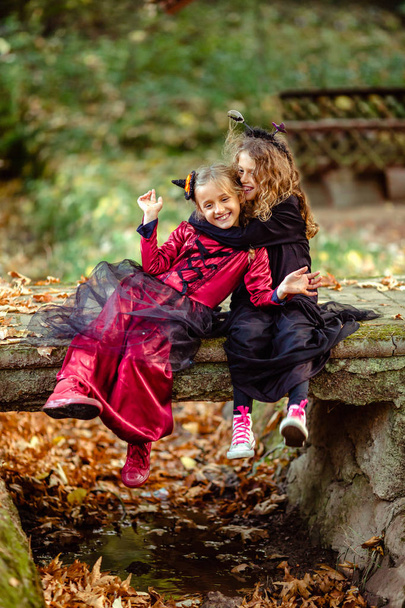 Deux filles en costumes et robes d'Halloween posant ensemble sur un fond de bois   - Photo, image