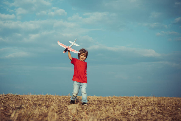 Child in the village with plane in his hands. Retro style airplane on nature background. Child boy toddler playing with toy airplane and dreaming future. Sweet childhood. Concept kids and nature. - Photo, Image