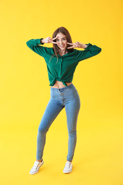 Beautiful young woman showing victory gesture on color background - Photo, image