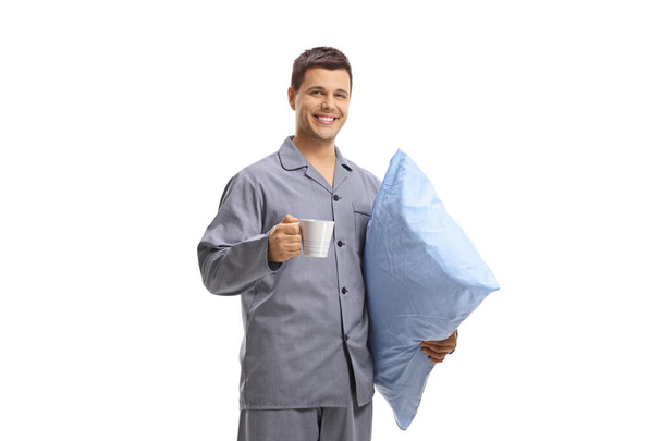 Guy in pajamas holding a pillow and a cup - Фото, изображение