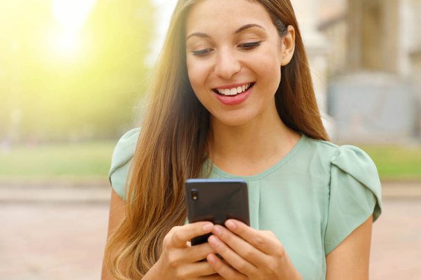 Detailní záběr krásné usměvavé ženy psaní na chytrý telefon venku. - Fotografie, Obrázek