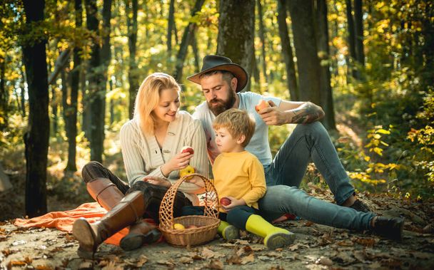 Picnic in nature. Country style family. Meaning of happy family. United with nature. Family day concept. Happy family with kid boy relaxing while hiking in forest. Mother father and small son picnic. - Zdjęcie, obraz