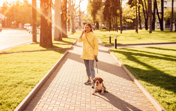 Cheerful woman with dog speaking on phone in park - Photo, Image