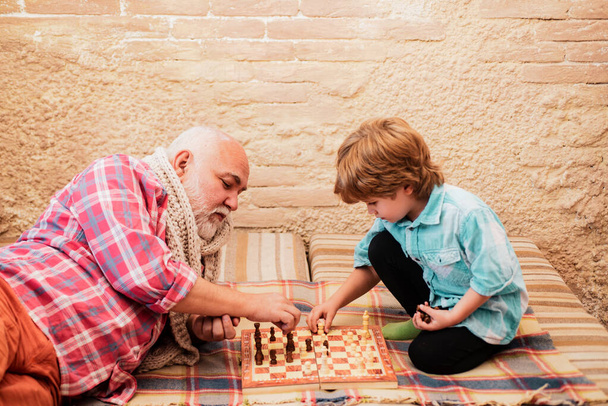 Generations. Checkmate. Senior man teaching his grandson to play chess. Chessman. Chess piece. - Фото, изображение