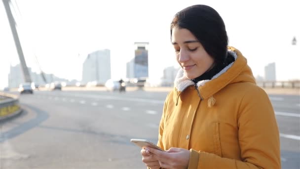 schöne Mädchen schreibt eine Nachricht auf ein Smartphone. Zeitlupe. Fahrbahn im Hintergrund - Filmmaterial, Video