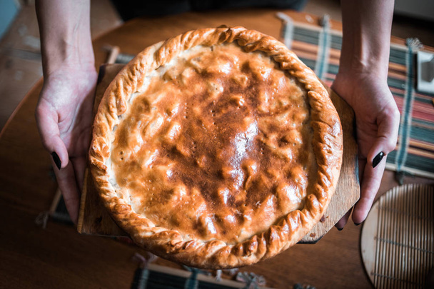 female hands hold a fresh hot apple pie in the kitchen. made with your own hands - 写真・画像