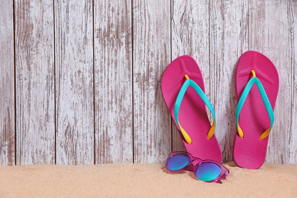 Bright flip flops and sunglasses on sand near wooden wall, space for text. Summer beach accessories - Photo, Image