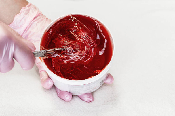 Beautician toma pasta shugaring transparente roja de una ca blanca
 - Foto, imagen